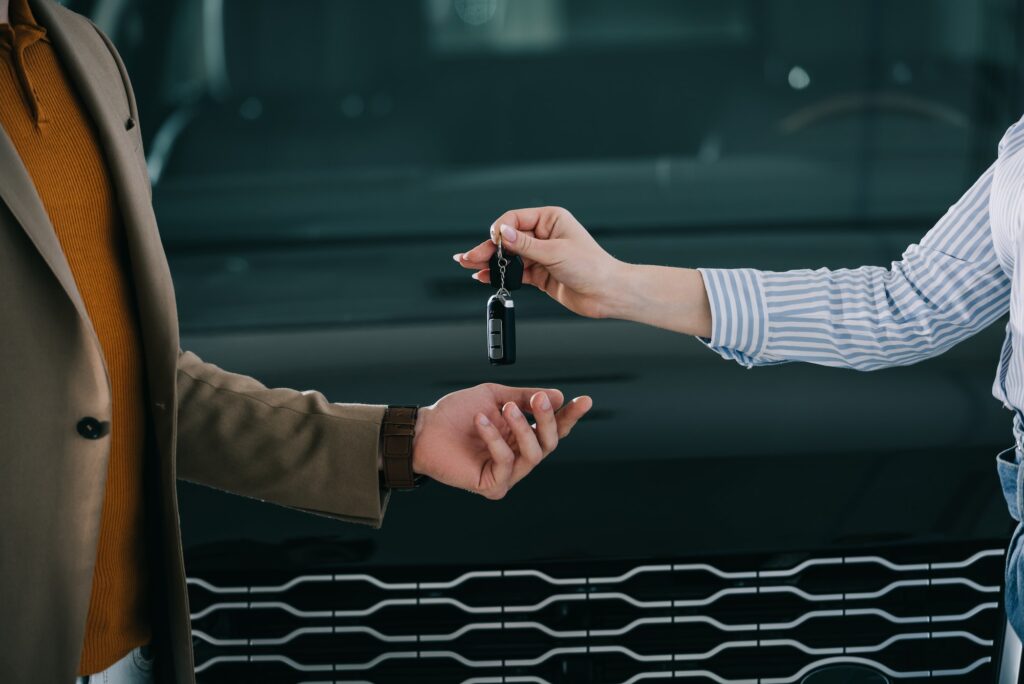 cropped view of car dealer giving key to man in car showroom