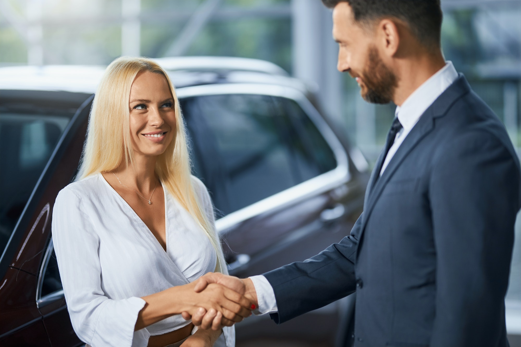 Car dealer shaking hands woman after car purchase