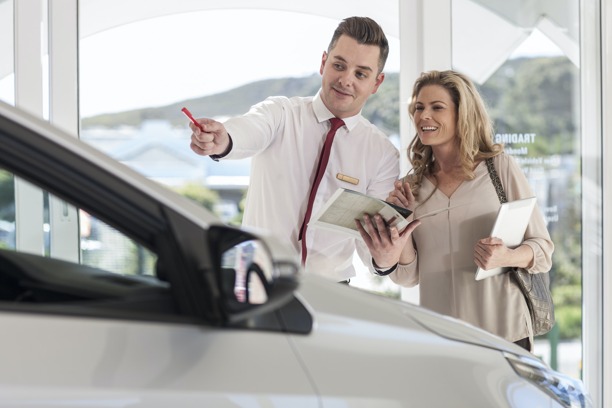Car dealer showing new car to woman in showroom