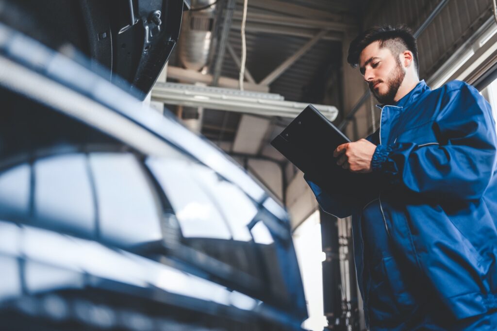 Car mechanic writes repair plan on clipboard. Auto service worker male